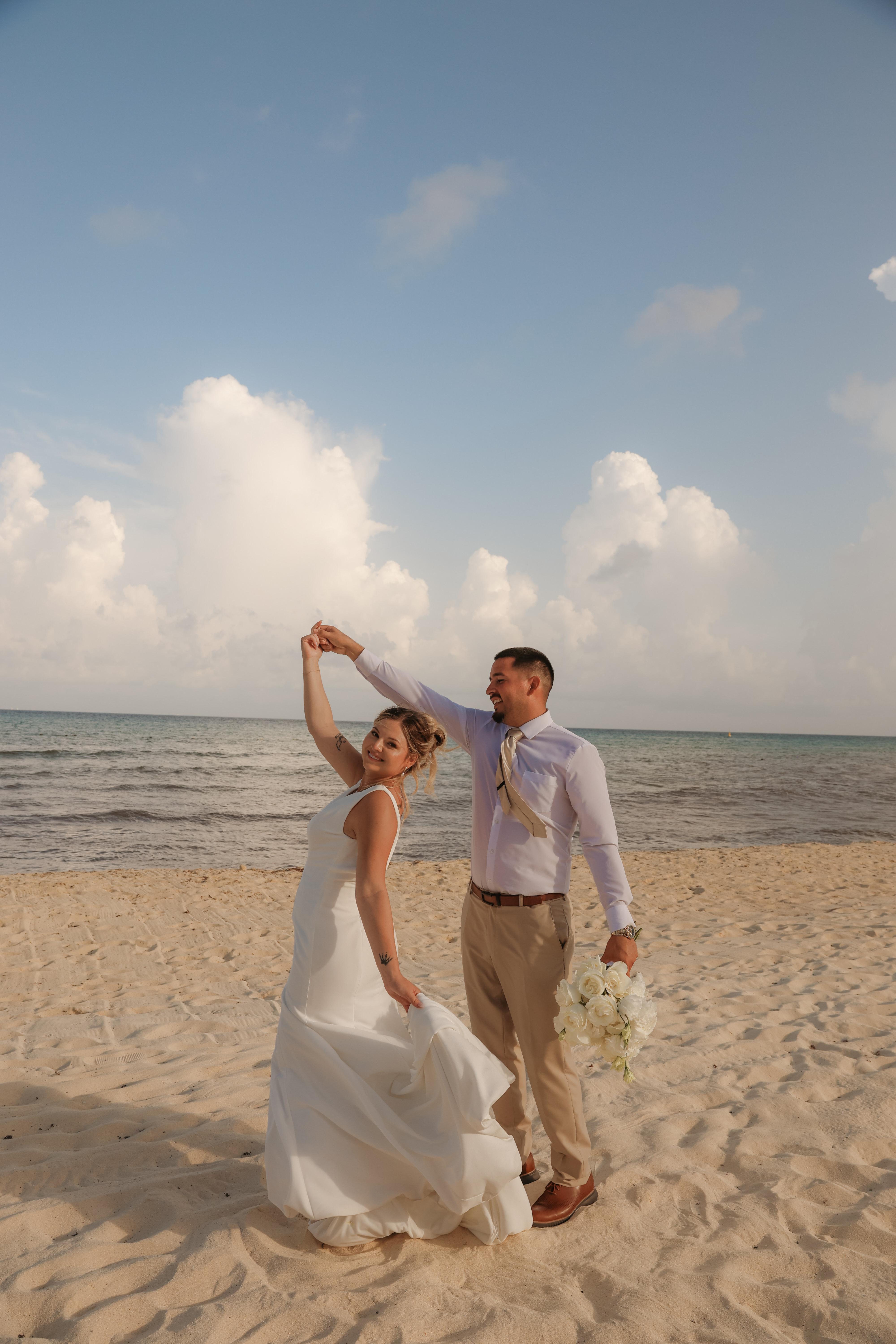 April and Javiert dance in wedding attire on a sandy beach, enjoying their destination wedding by the ocean.