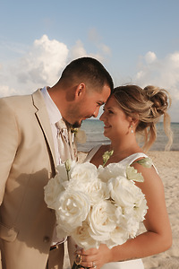 April and Javiert smiling at their destination wedding on the beach, holding a bouquet of white roses.