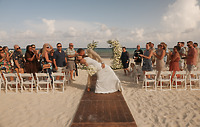 April and Javiert kiss at their destination wedding on the beach while guests watch and celebrate.