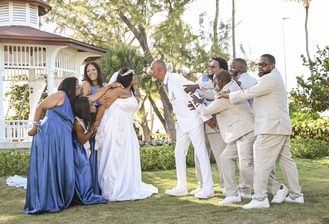 At a destination wedding, the bridal party playfully pulls Richard and Keily apart near an outdoor gazebo.