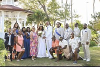 A destination wedding party in formal attire poses outdoors by a white gazebo.