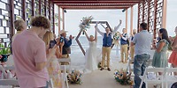 Bride and groom celebrate at the altar during a destination wedding as guests applaud outdoors.