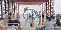 A couple exchange vows at their destination wedding, held outdoors with the ocean as a scenic backdrop.