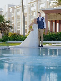 Bride and groom at their destination wedding, standing by a pool with a building behind them.