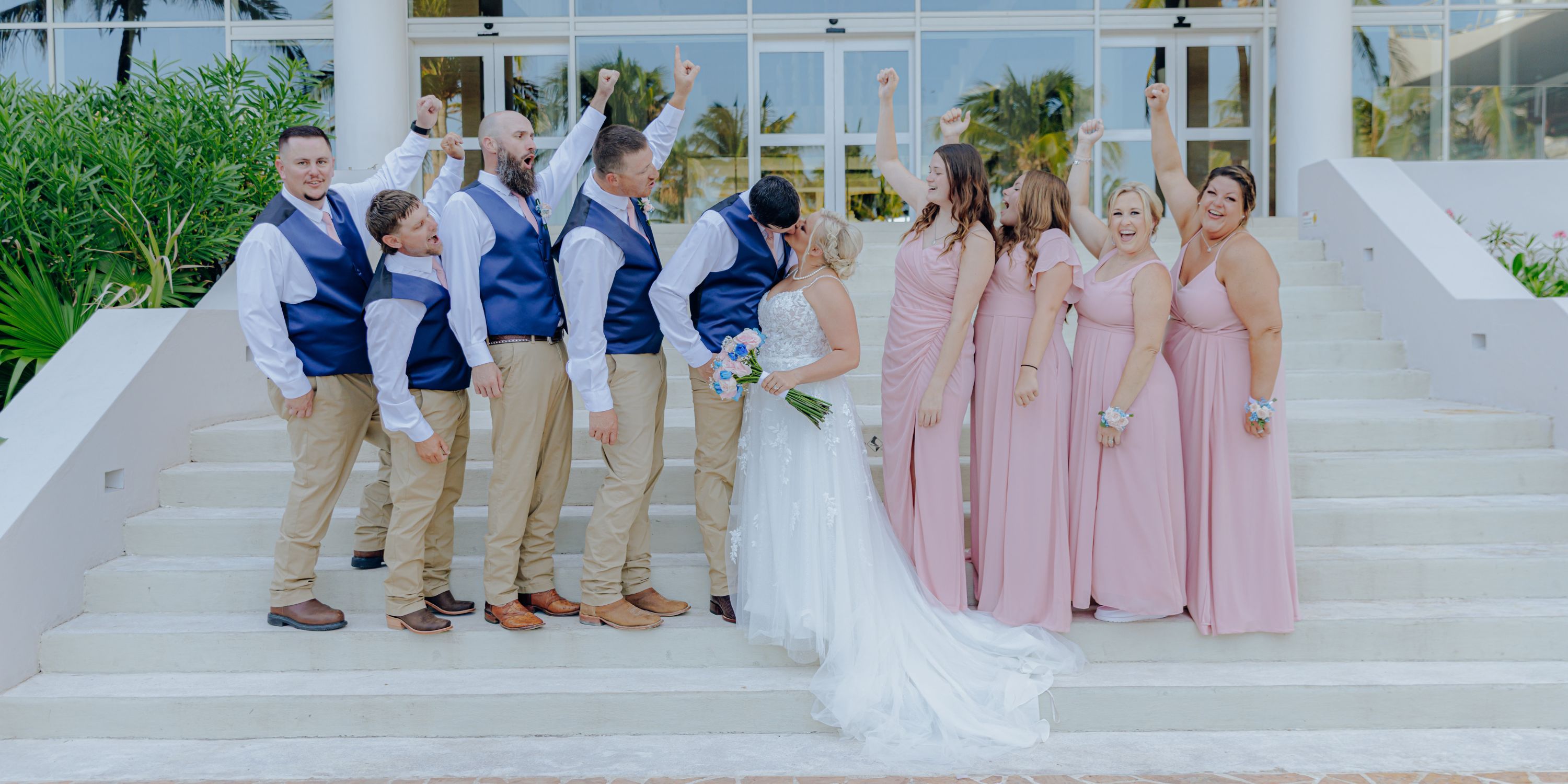 Newlyweds share a kiss on the steps at their destination wedding, cheered on by bridesmaids and groomsmen.