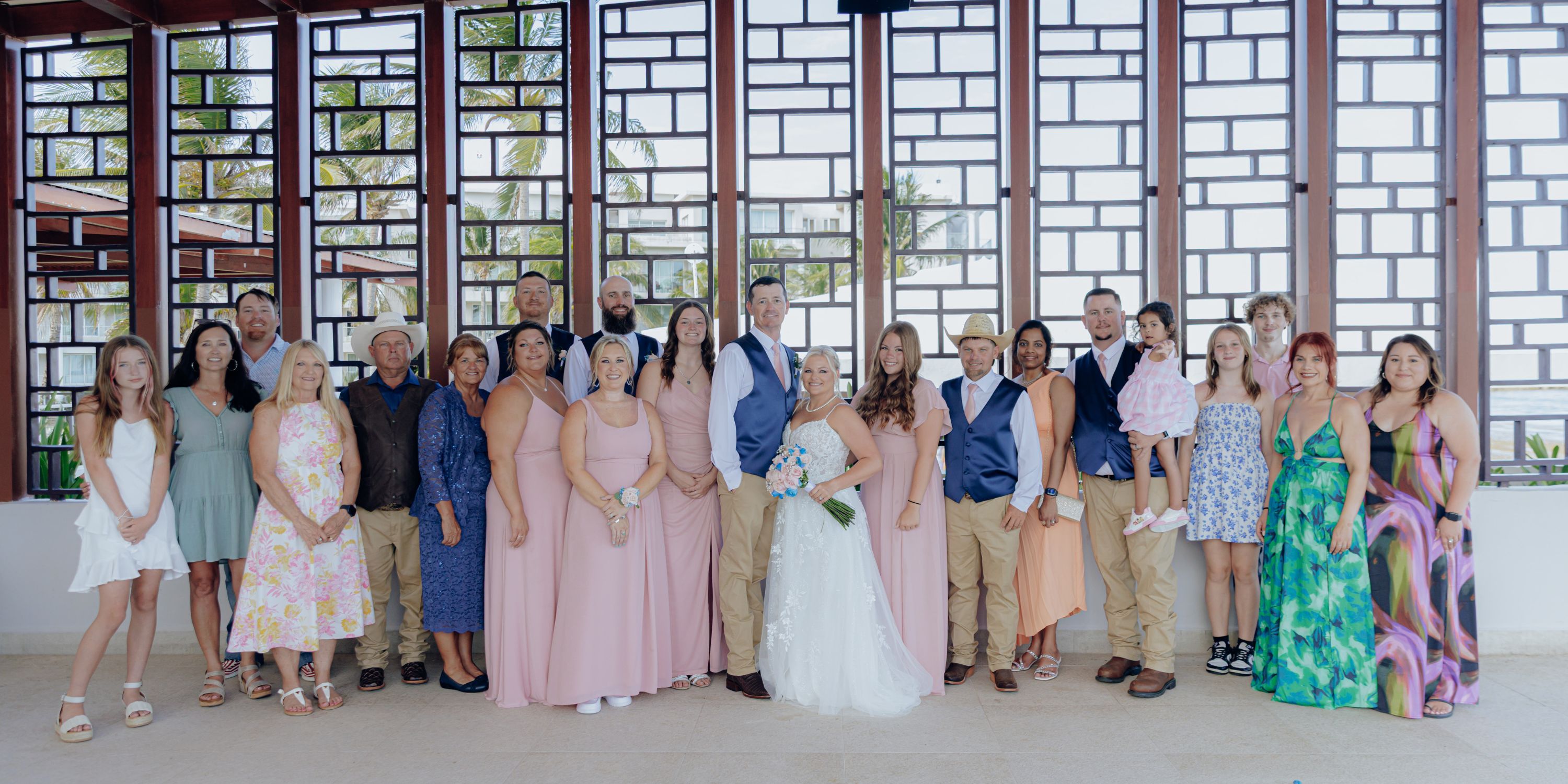 A destination wedding group poses inside before tall windows with striking geometric frames.