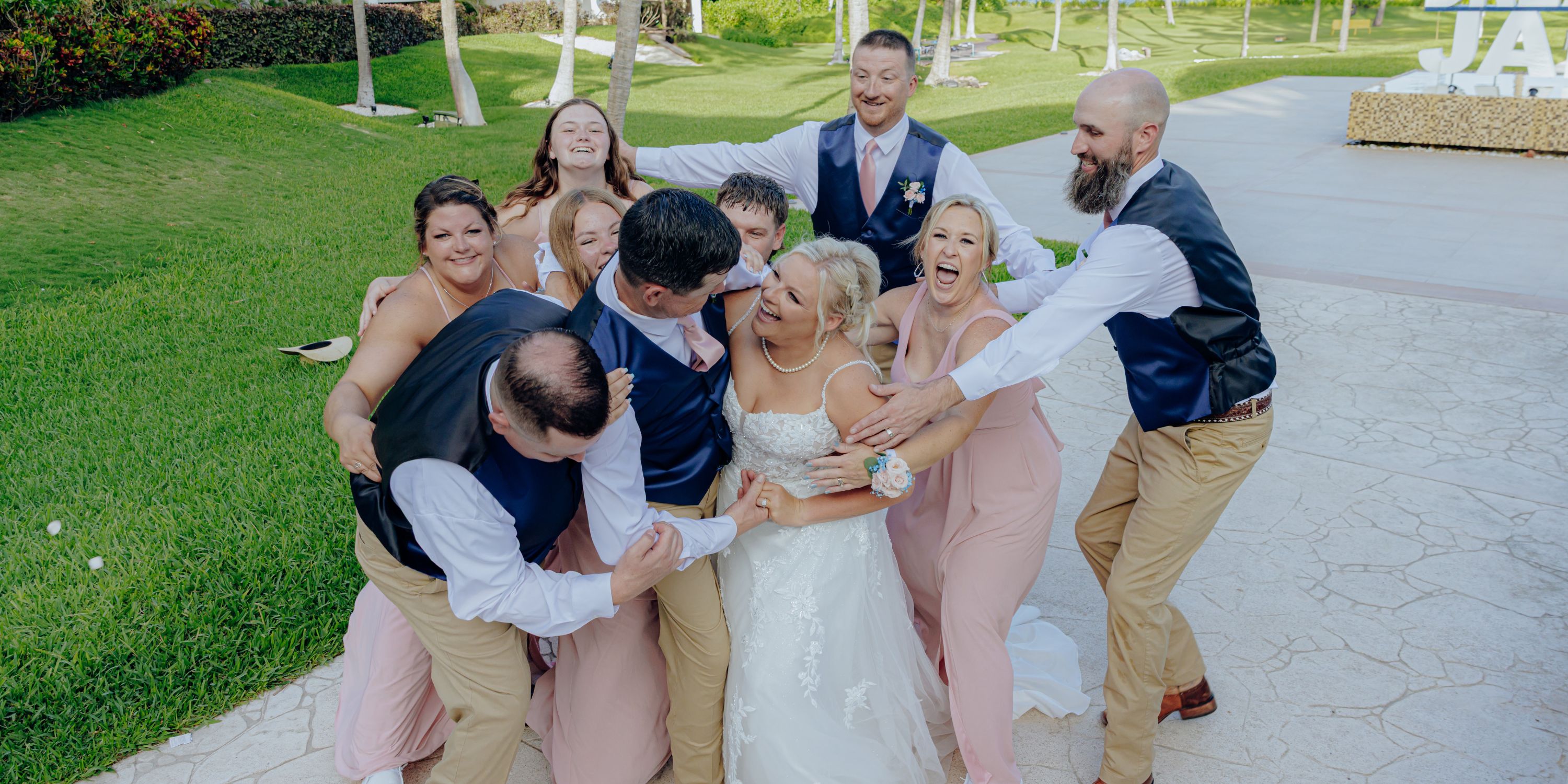 A joyful destination wedding party laughing and hugging together outdoors under bright sunshine.