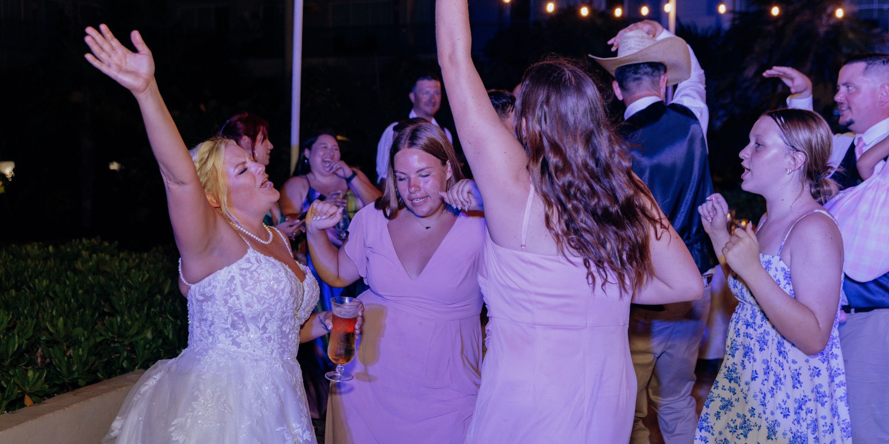 Guests in formal attire join the bride dancing and celebrating at an outdoor destination wedding event.