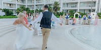A bride and groom make their entrance at a poolside destination wedding as guests watch and applaud.