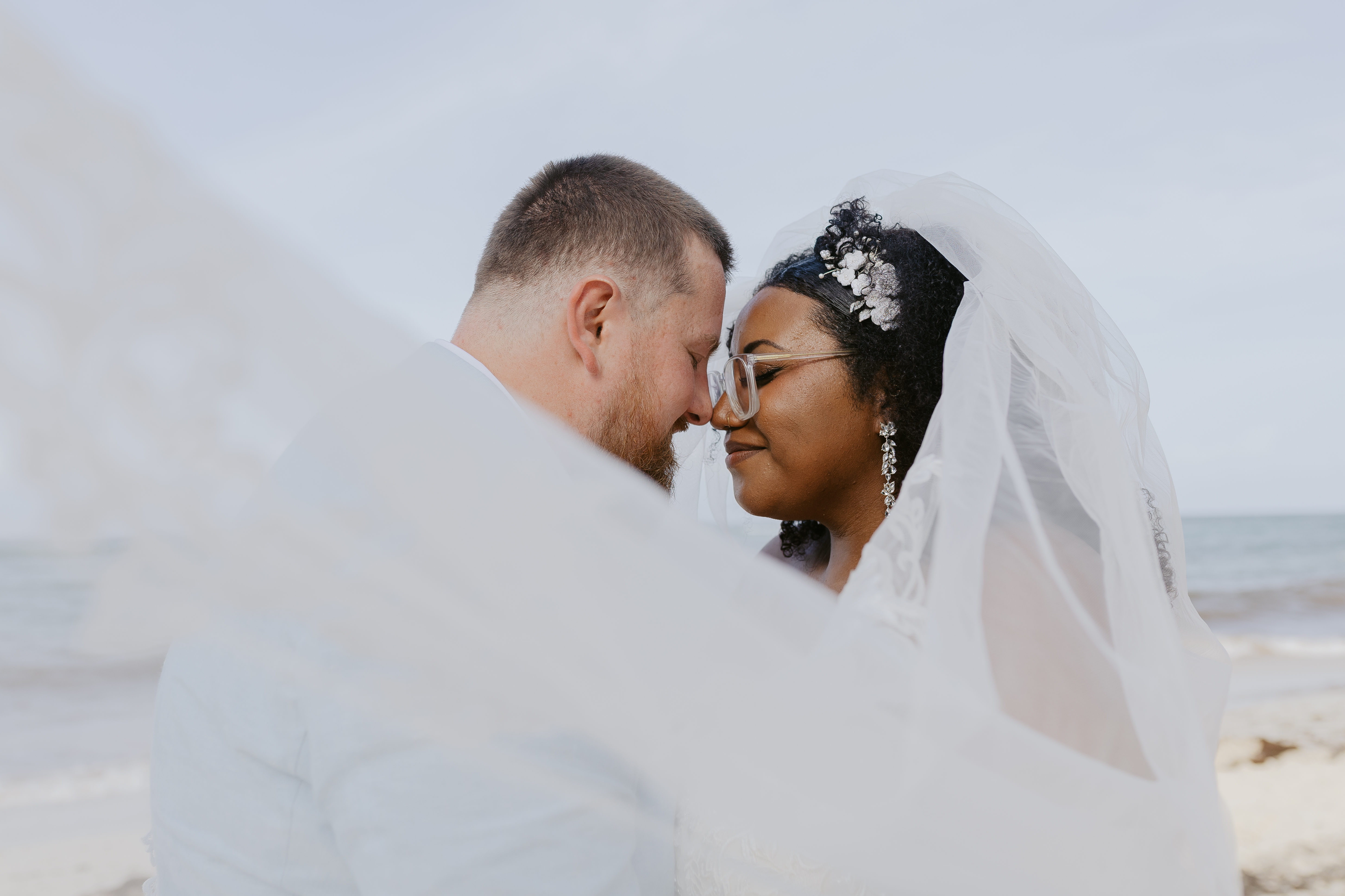 Alicia and Brian share a tender moment under a veil on the beach at their destination wedding.