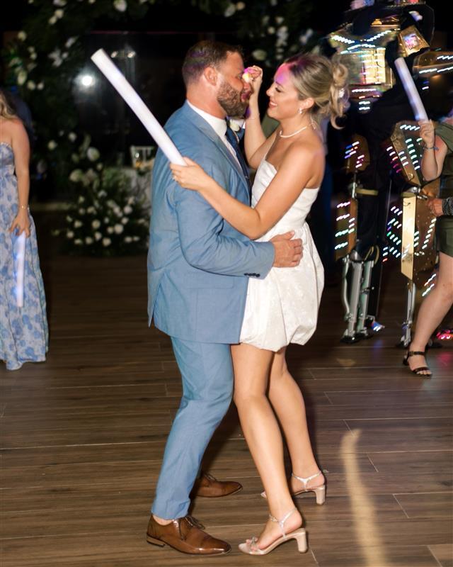 Teya and Charles (Copy) dance at a destination wedding, she in white, he in blue, on a wooden floor.