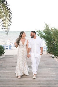 Teya and Charles (Copy) walk hand in hand on a wooden path by the beach at their destination wedding.