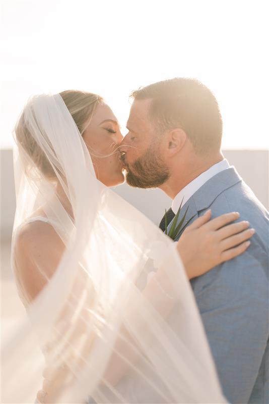 Teya and Charles share a kiss beneath a veil in soft sunlight at their destination wedding.