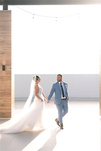 Teya and Charles holding hands, walking indoors in bright light at their destination wedding.