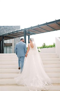 Teya and Charles holding hands, walking up outdoor steps under a modern pergola at their wedding.