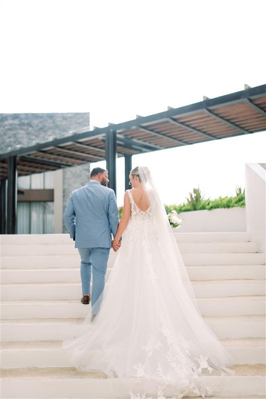Teya and Charles holding hands, walking up outdoor steps under a modern pergola at their wedding.