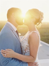 Teya and Charles share a kiss at sunset during their destination wedding, golden sunlight glowing between them.