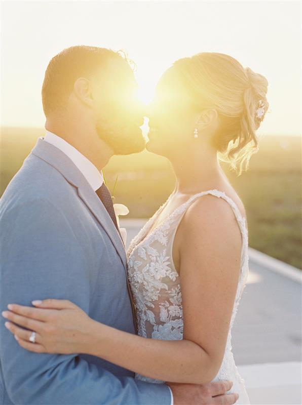 Teya and Charles share a kiss at sunset during their destination wedding, golden sunlight glowing between them.