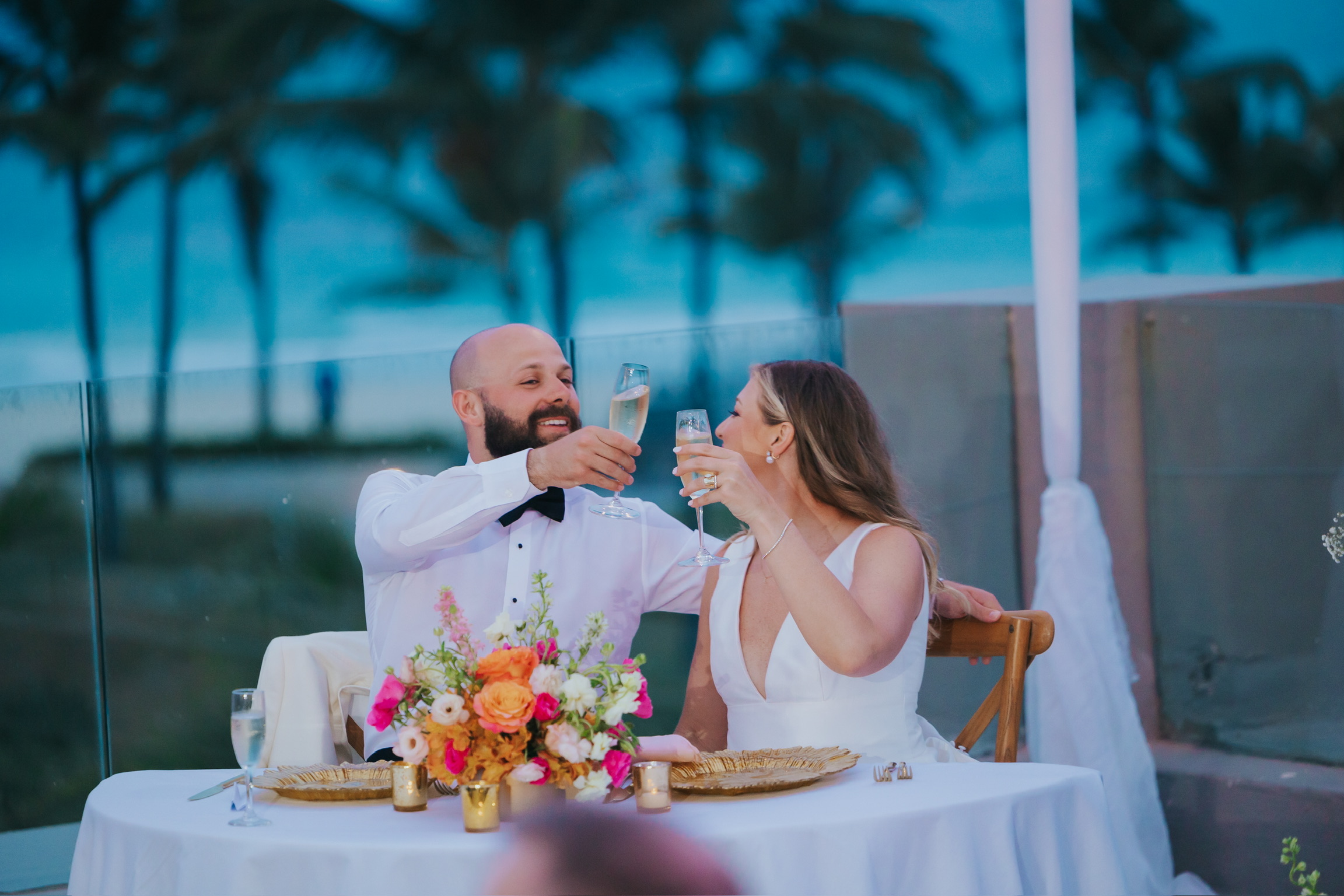Billi and Trevor toast with champagne at a beautifully decorated destination wedding table outdoors.