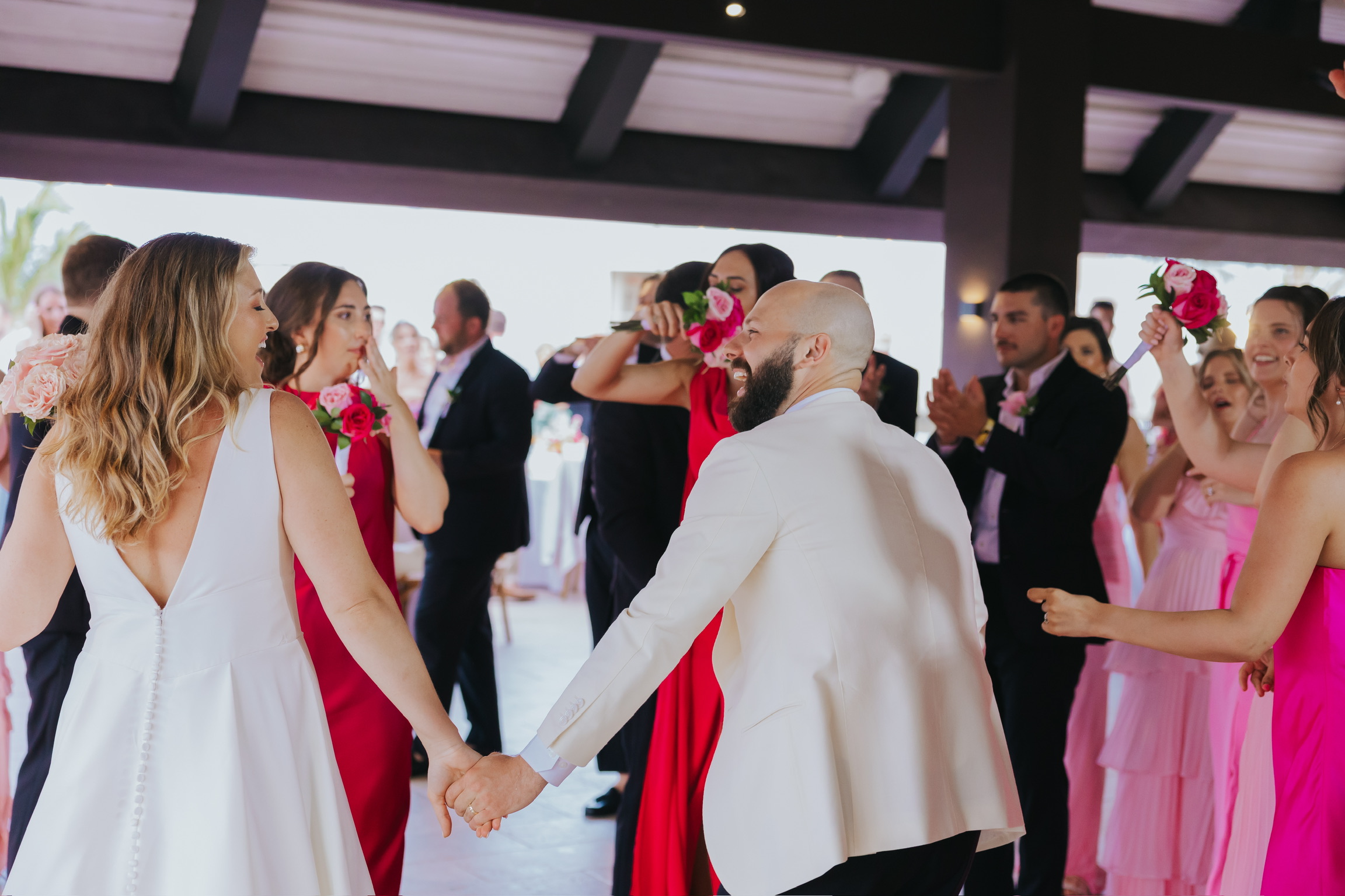 Billi and Trevor hold hands and dance together among guests at a lively destination wedding reception.