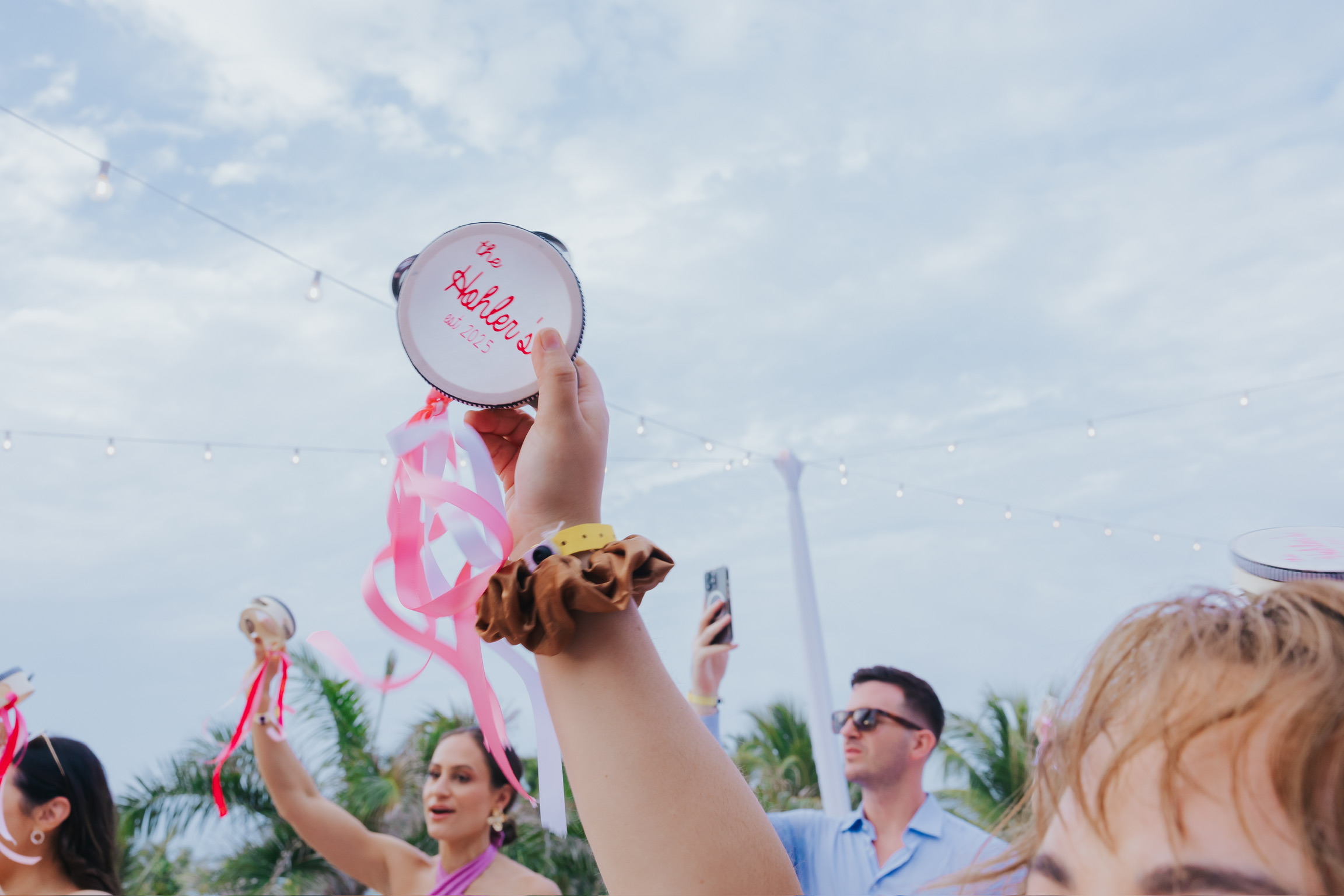 Person holds up a Billi and Trevor (Copy) tambourine at an outdoor destination wedding gathering.