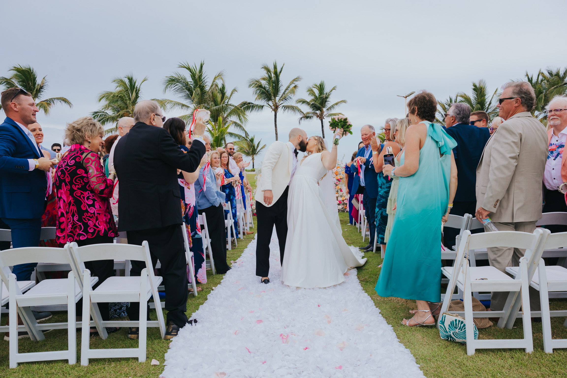 Billi and Trevor share a kiss at their destination wedding, guests cheering as they walk down the aisle.