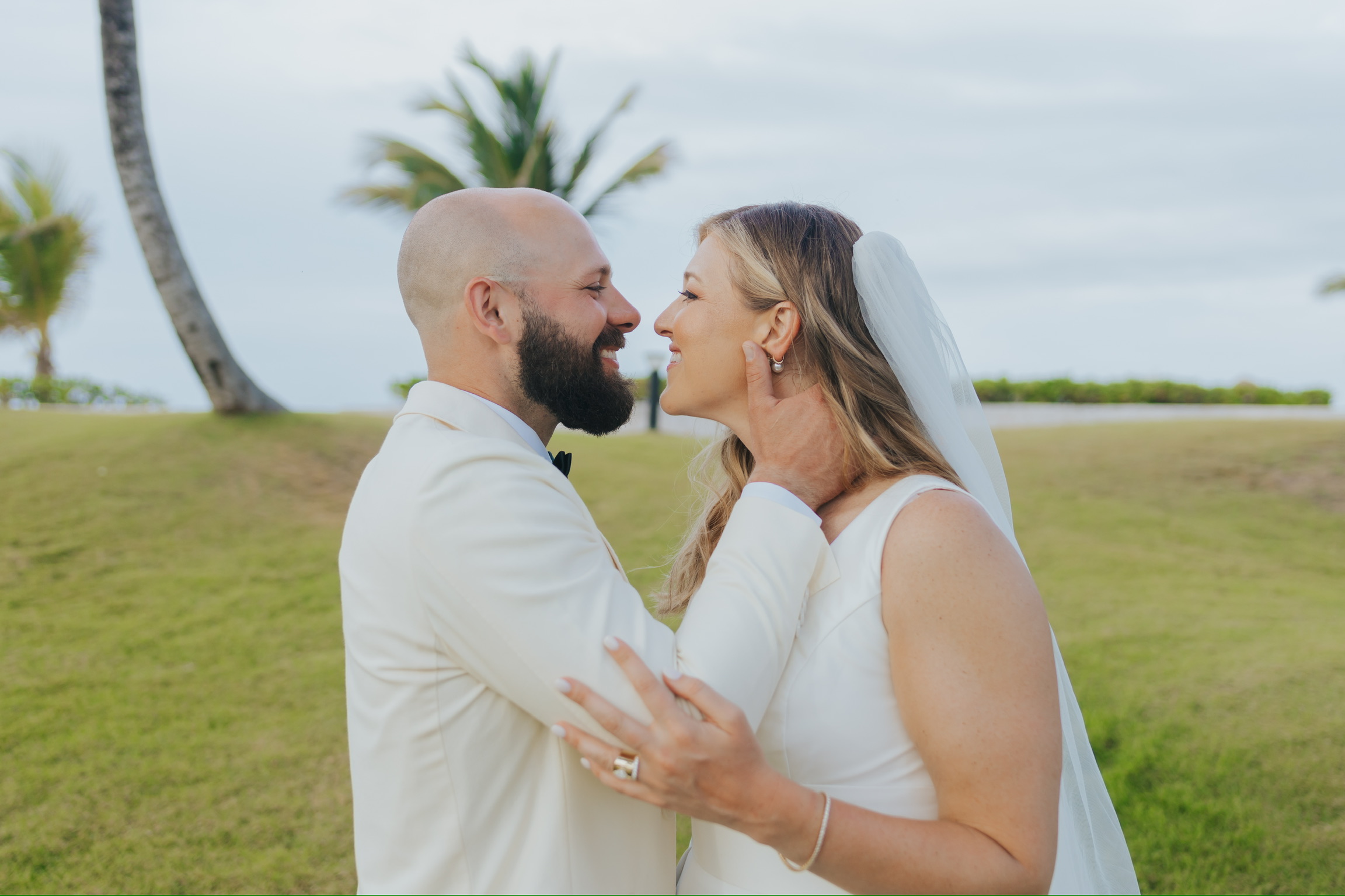 Billi and Trevor embrace and smile in wedding attire on a grassy lawn at their destination wedding.