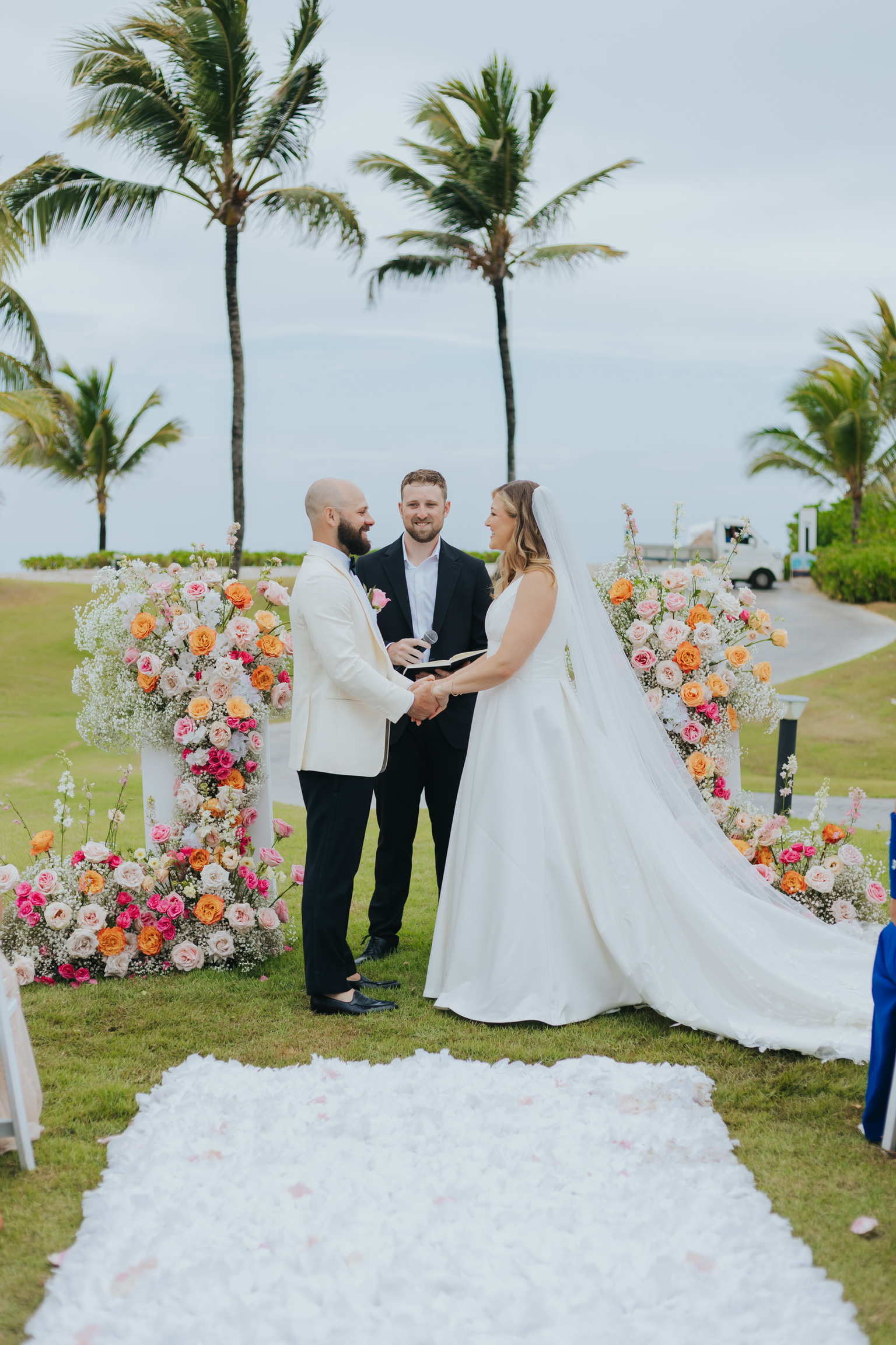 Billi and Trevor hold hands at their destination wedding, surrounded by beautiful floral decorations.