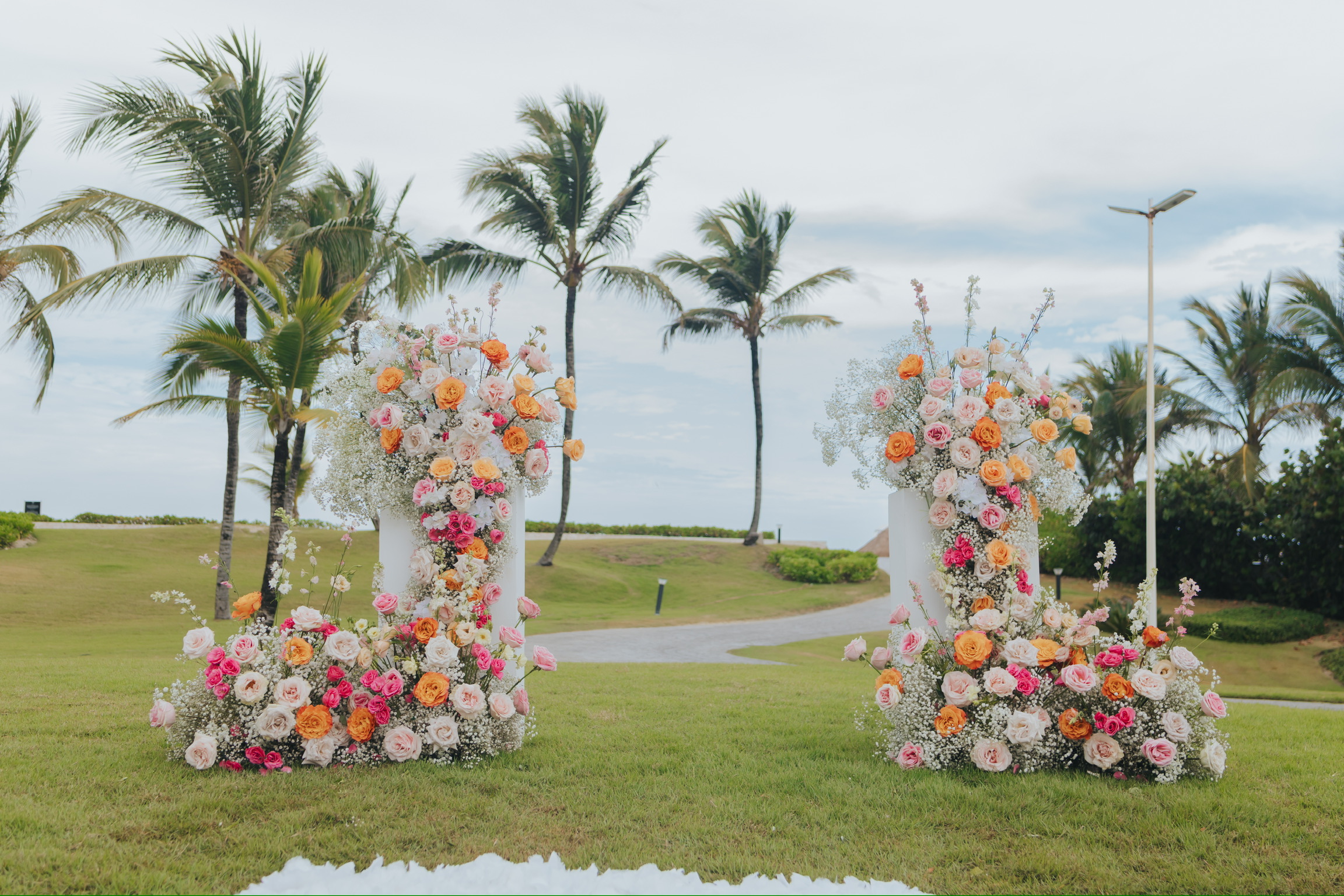 Two large wedding floral arrangements on grass with palm trees behind, perfect for a destination wedding.