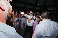 Man in Billi and Trevor (Copy) sunglasses holds a drink, pointing at camera during destination wedding.