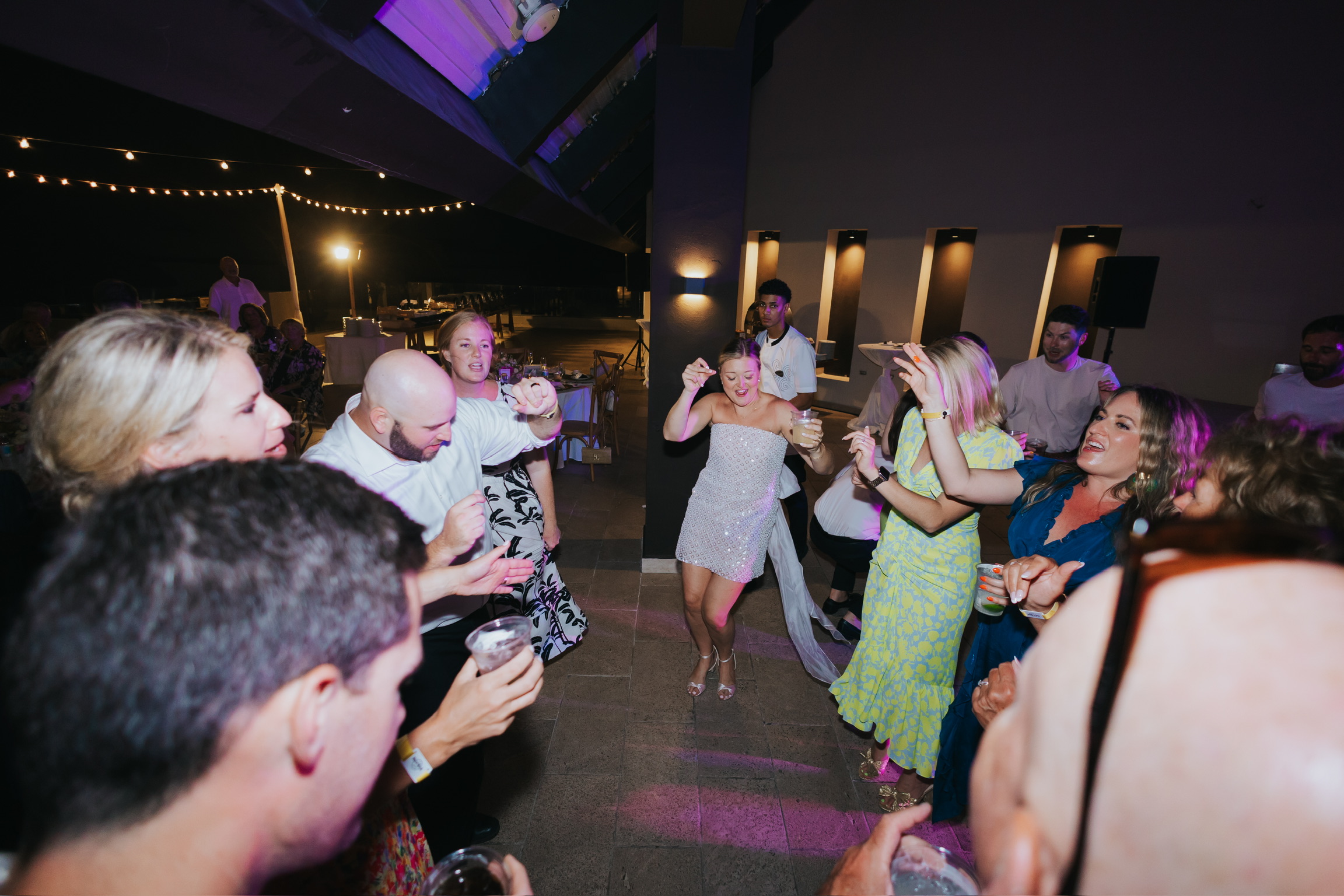 Guests celebrate a destination wedding indoors under string lights at night with Billi and Trevor.