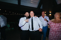 Billi and Trevor smile together at a destination wedding, posing with other guests in the background.