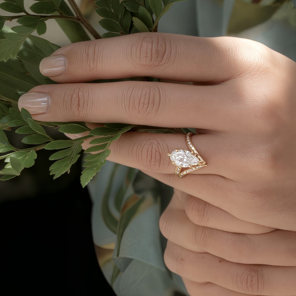 Close-up of a hand with a pear-shaped diamond wedding ring, holding green leaves at a destination wedding.