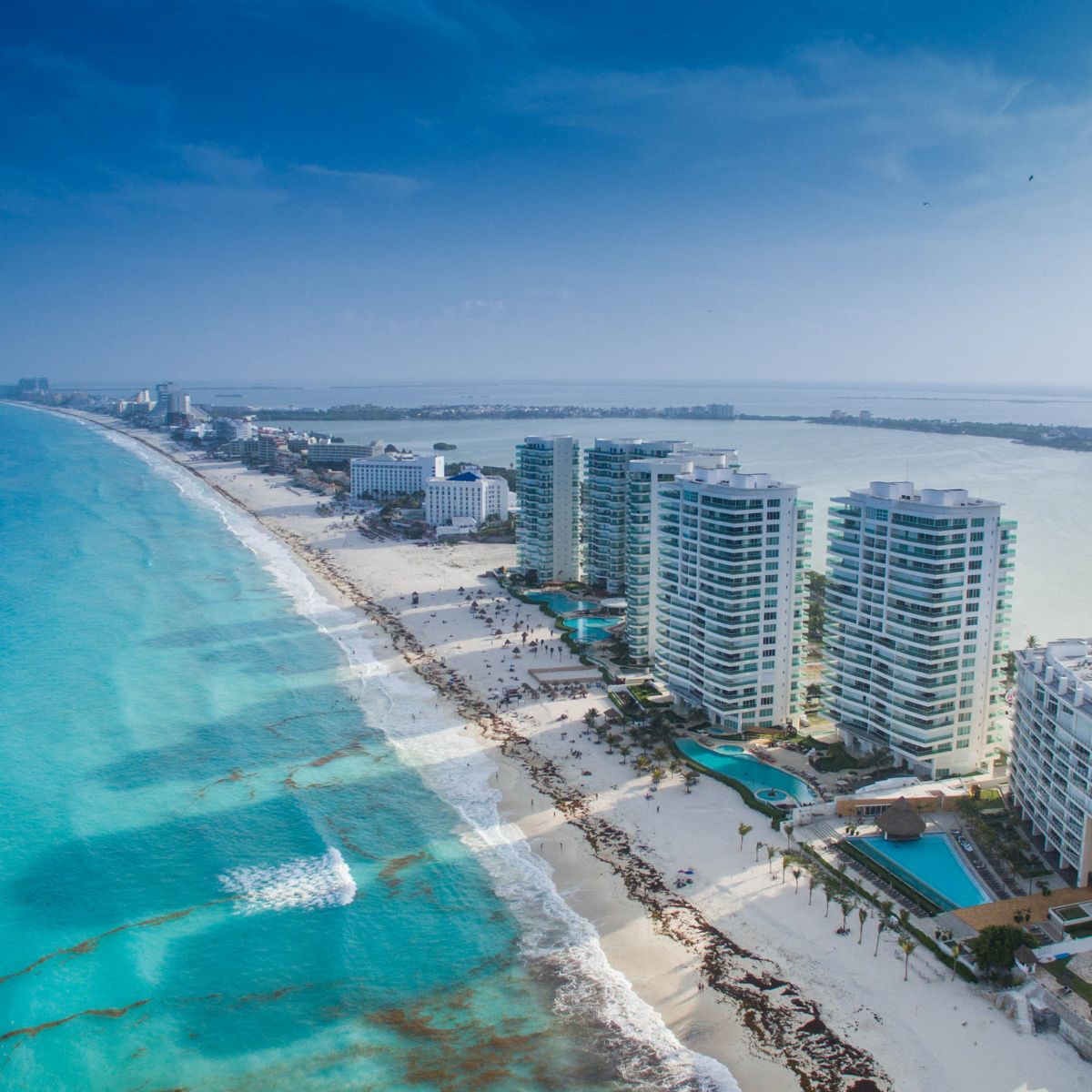 Aerial view of beachfront high-rise hotels by turquoise ocean, perfect for a destination wedding.