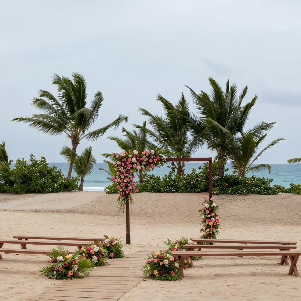 Wooden wedding arch with pink flowers on a sandy beach, perfect for a destination wedding, benches and palm trees behind.