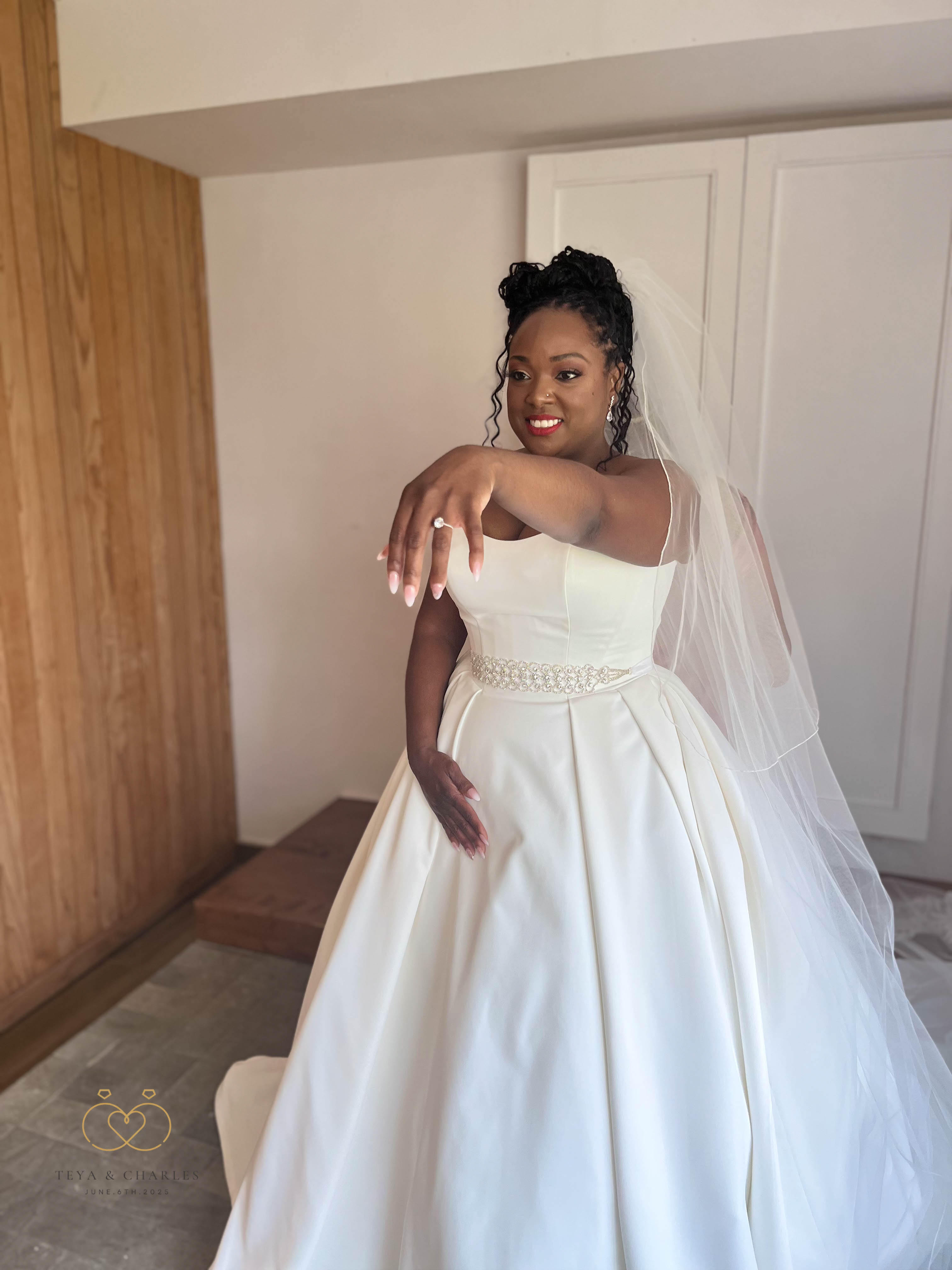 Teya, in a white wedding gown and veil, shows her engagement ring from Teya and Charles indoors.