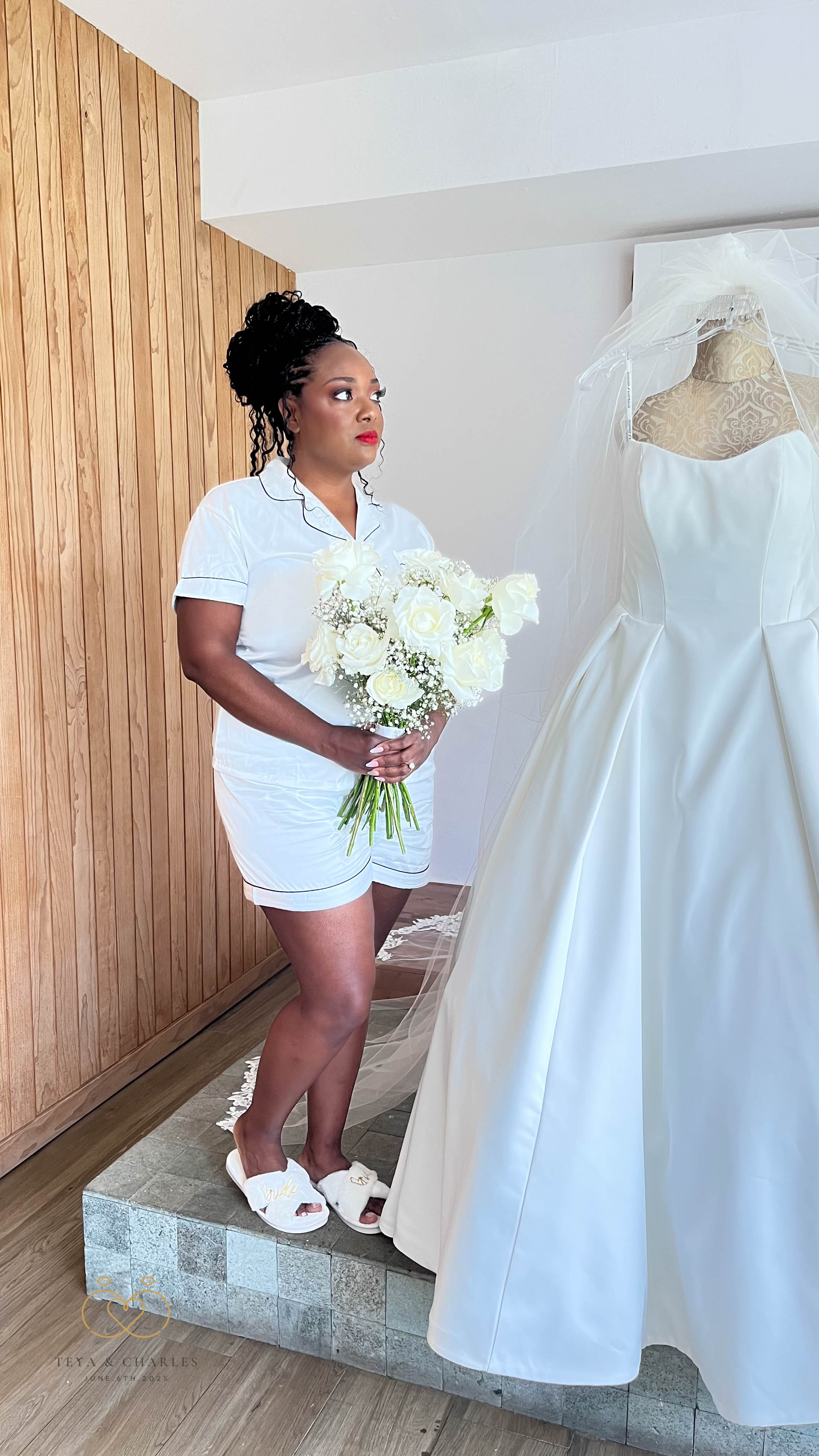 Woman in white pajamas holds a destination wedding bouquet by a wedding dress mannequin.