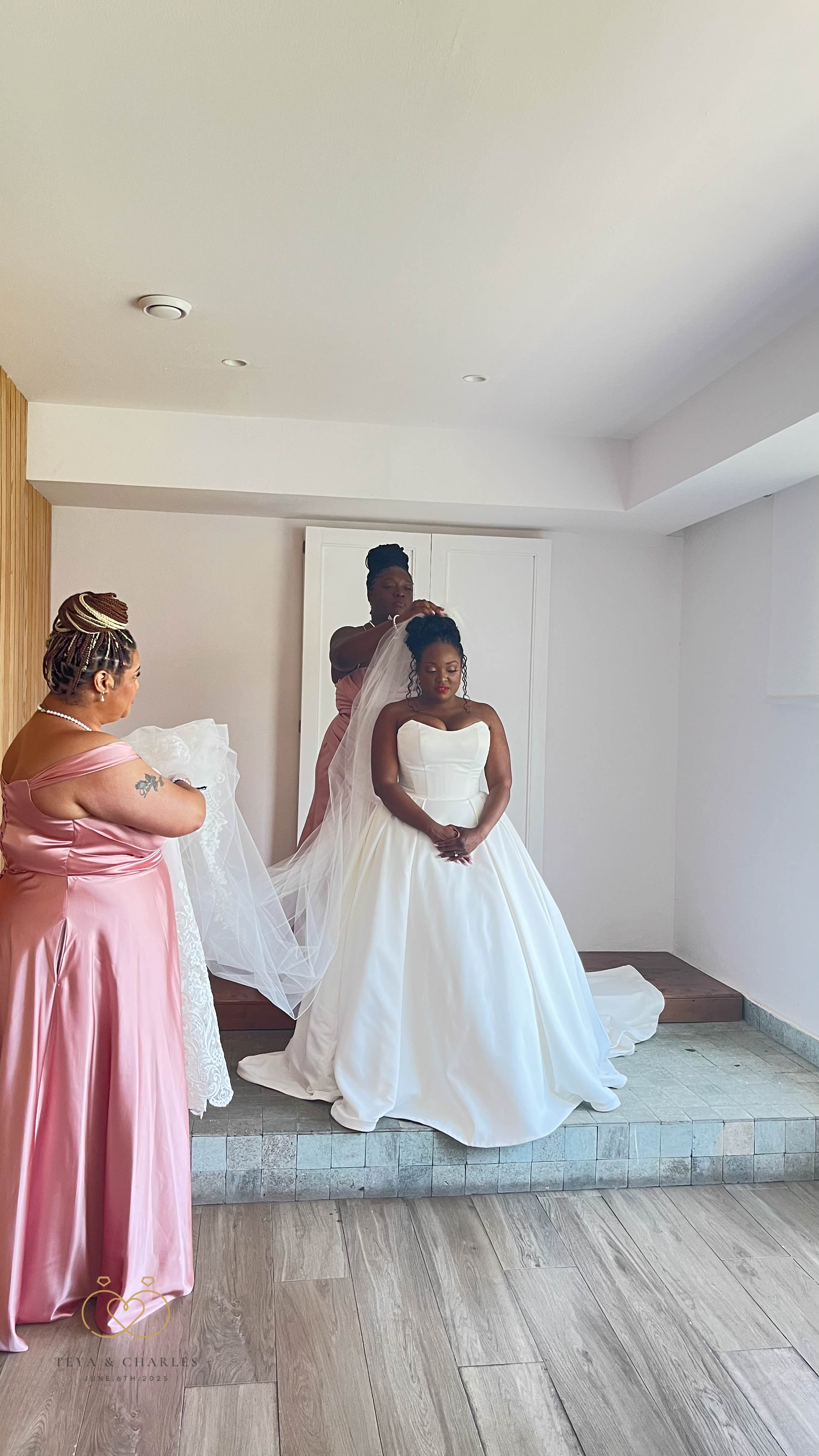 At a destination wedding, four women assist a bride in her white gown with adjusting her veil.
