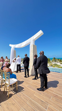 Iyana and Marcello’s destination wedding by the ocean, with guests seated beneath a white arch.