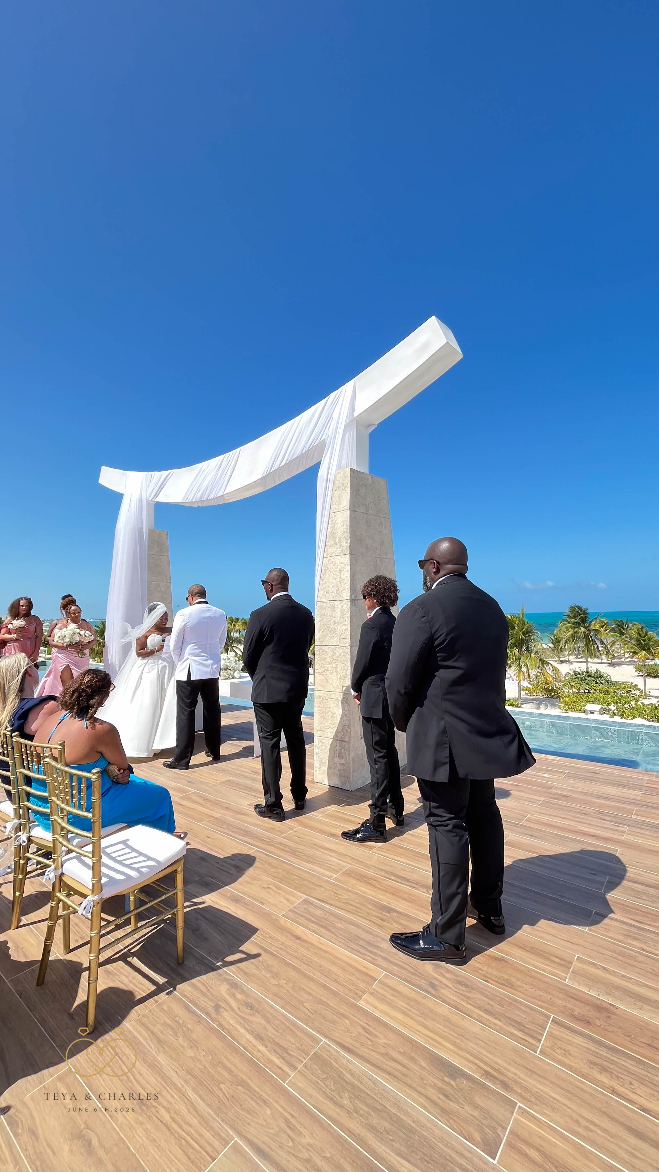 Iyana and Marcello’s destination wedding by the ocean, with guests seated beneath a white arch.
