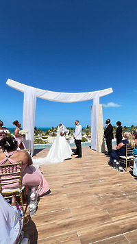 Iyana and Marcello stand beneath an arch at their destination wedding by the oceanfront.