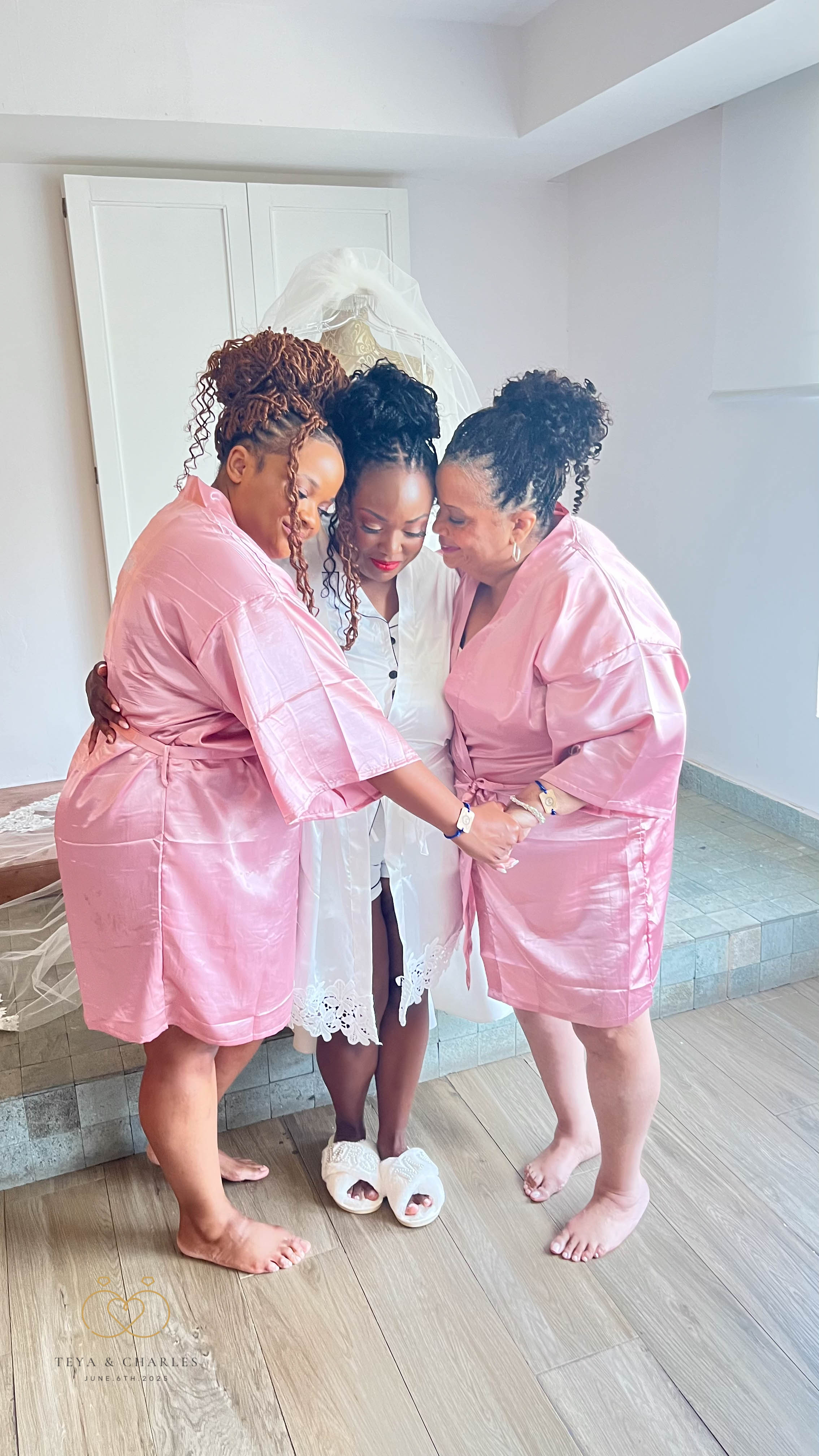 Three women in robes embrace and hold hands in a circle at a destination wedding for Iyana and Marcello.