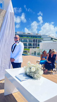 Man in white tux at Iyana and Marcello destination wedding, guests seated outdoors behind him.