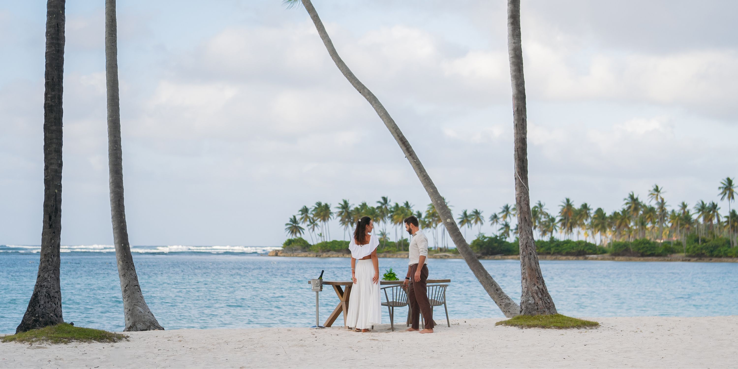 Two people stand by a table at Wyndham Alltra Punta Cana during a destination wedding, beach behind.