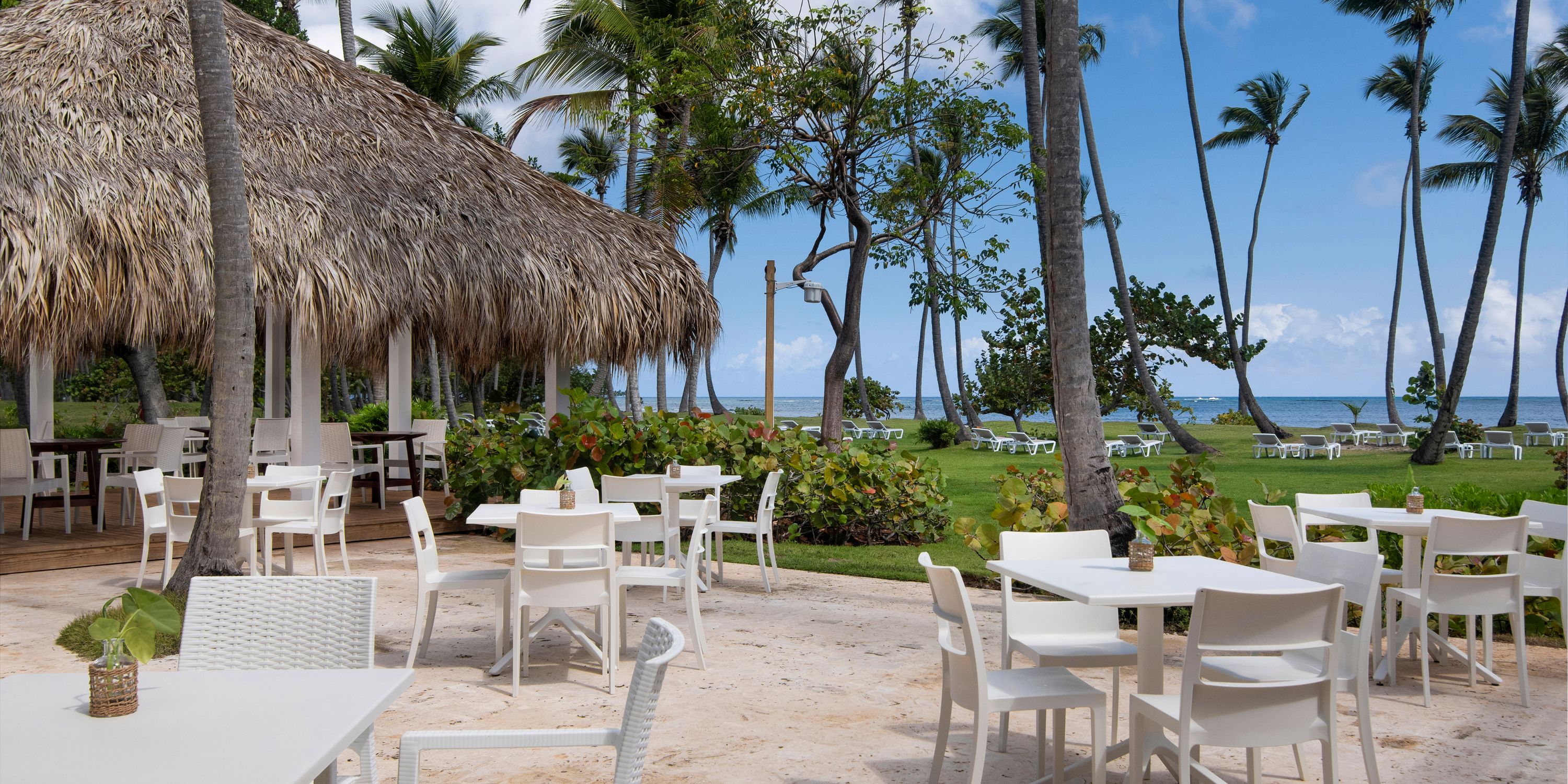 Outdoor dining set for a destination wedding at Wyndham Alltra Punta Cana, white tables, palm trees, ocean.
