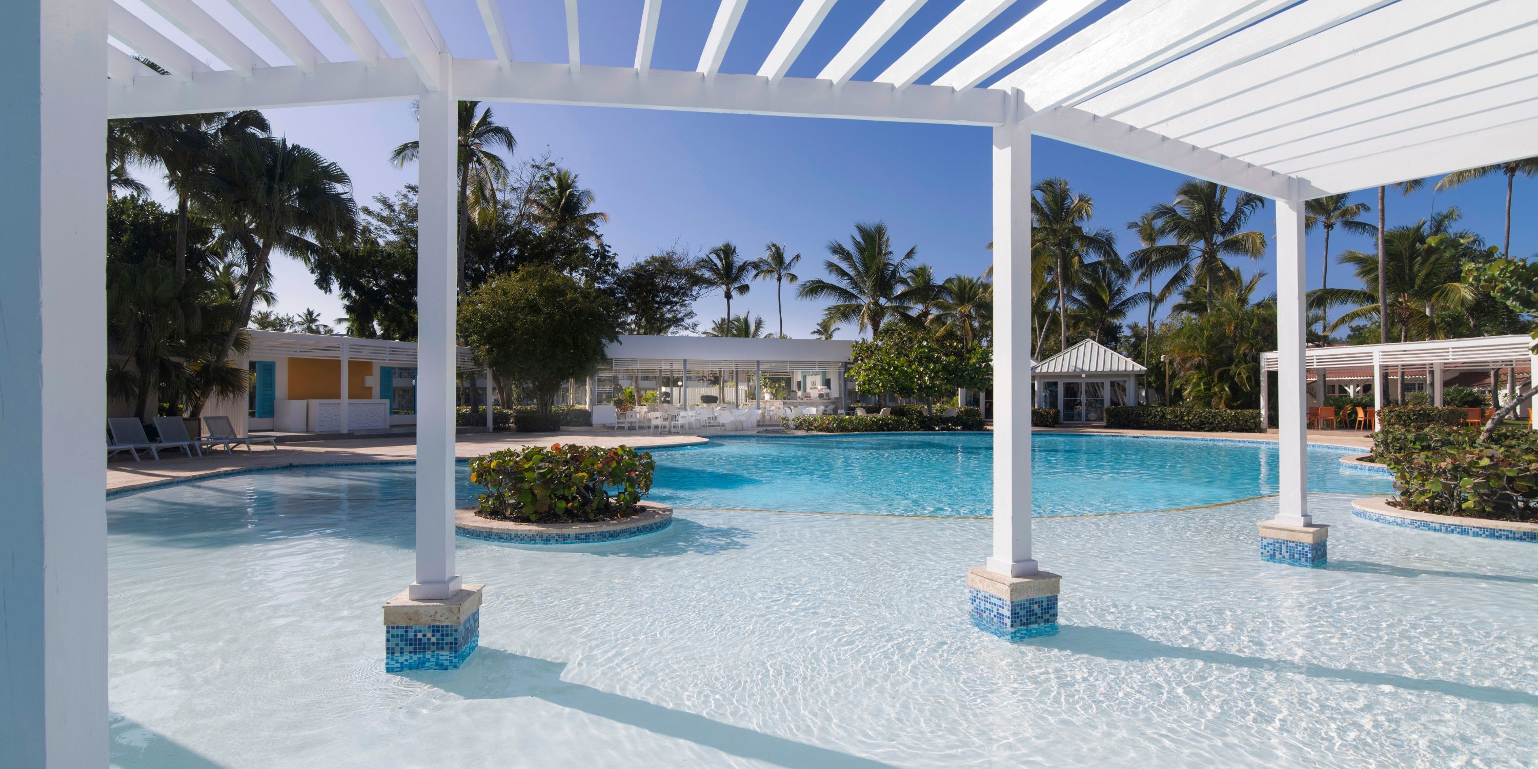 Wyndham Alltra Punta Cana: Outdoor pool with pergola, palm trees, white buildings—perfect for a wedding.