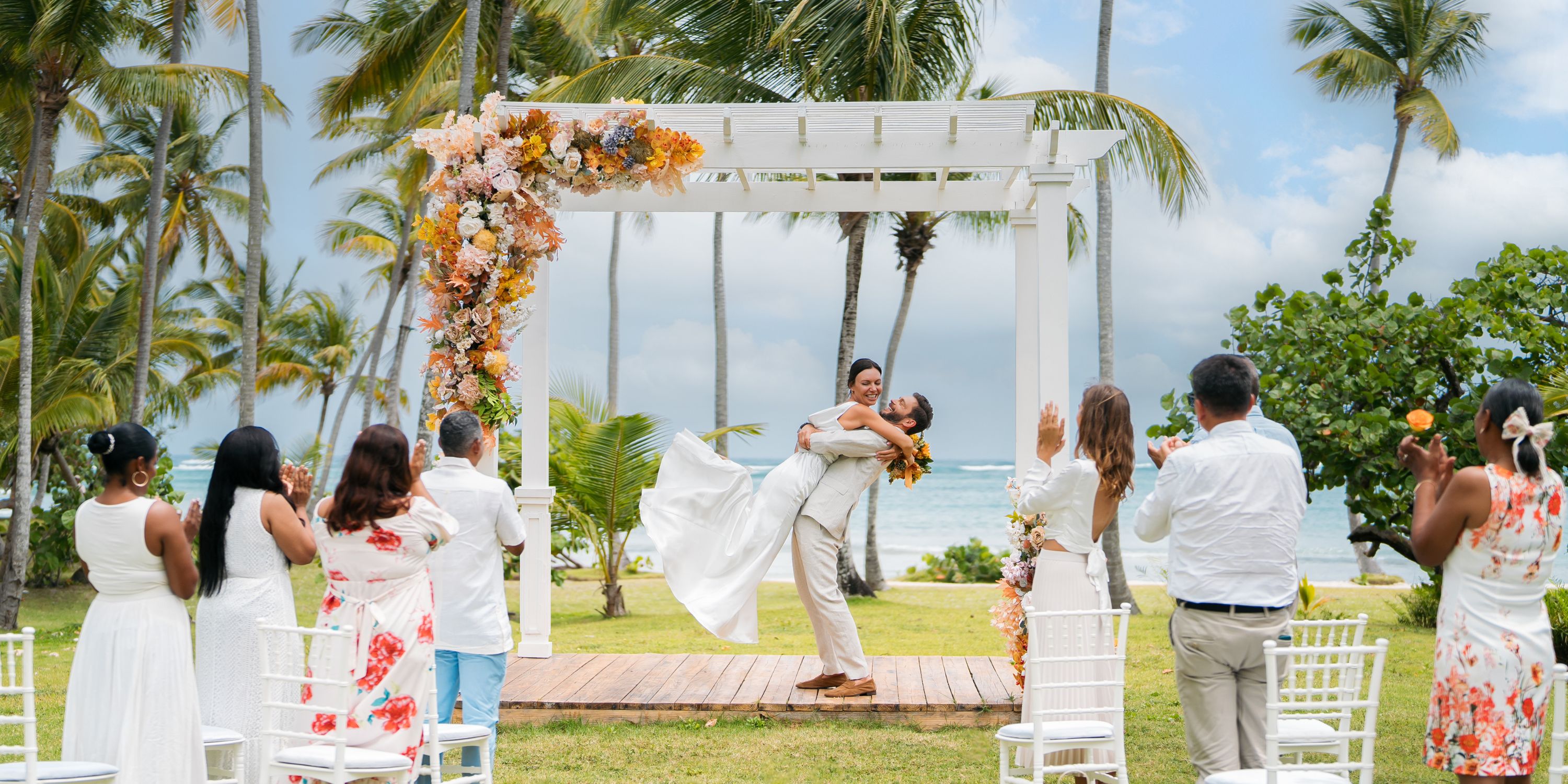 During a dreamy destination wedding at Wyndham Alltra Punta Cana, the groom lifts the bride under a floral arch.