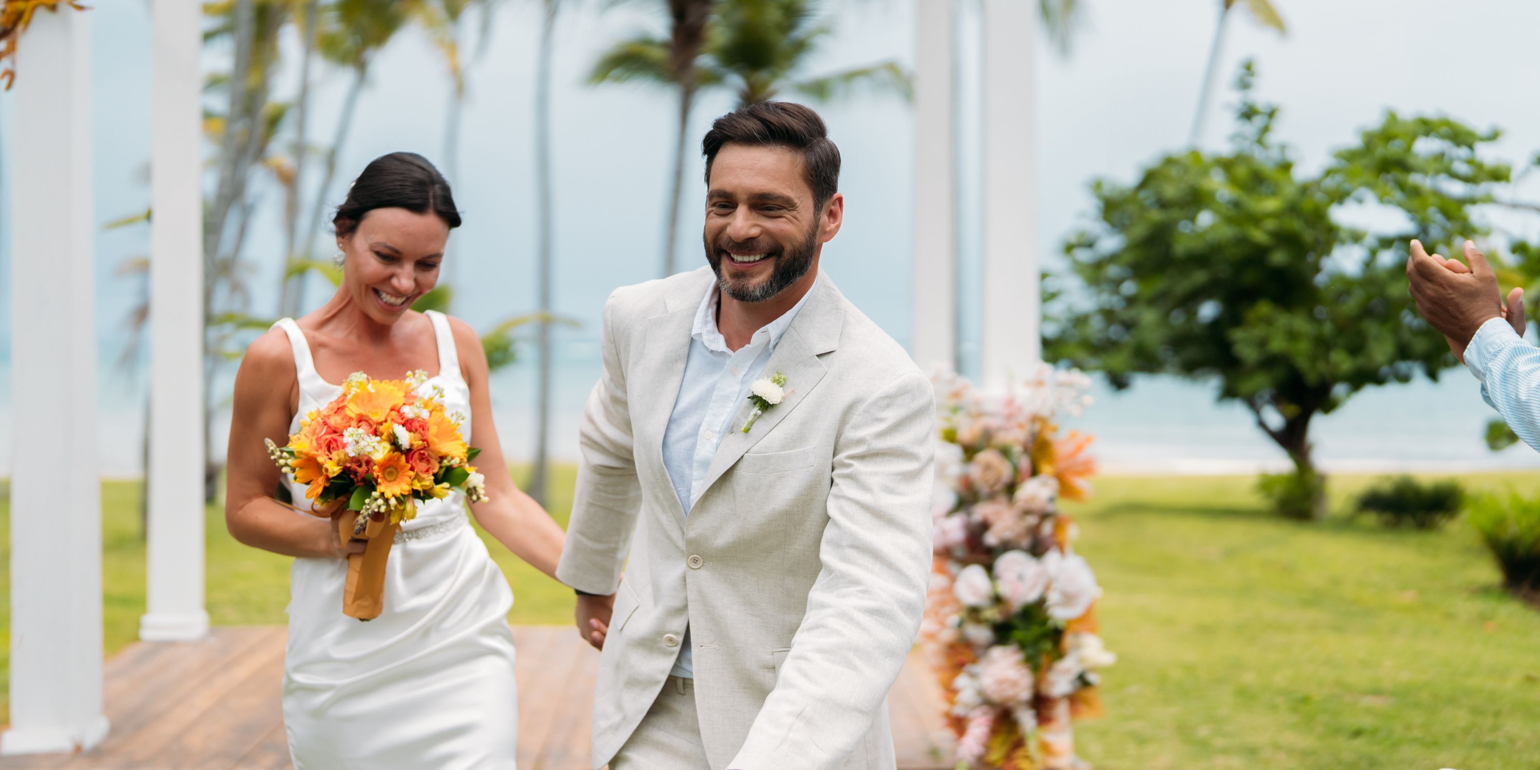A bride and groom smile and hold hands outside Wyndham Alltra Punta Cana after their destination wedding.