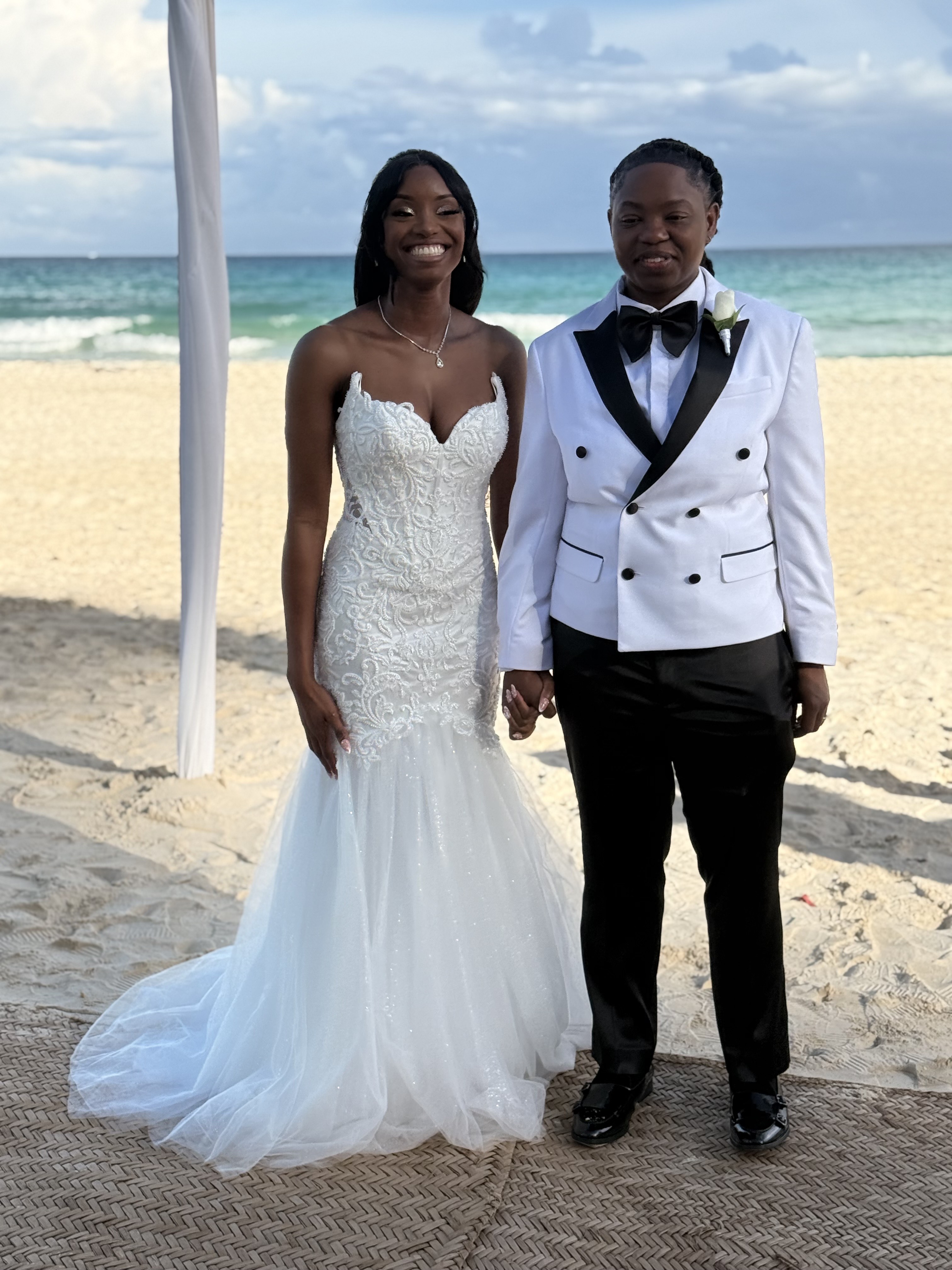 Kathleen and Lucas pose on a beach in wedding attire at their destination wedding by the ocean.