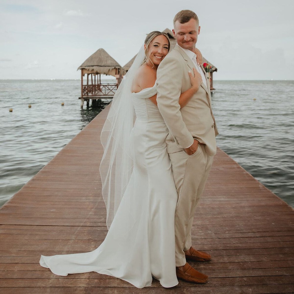 Kaitlyn and Chad, dressed in white, stand back-to-back on a dock at their destination wedding.